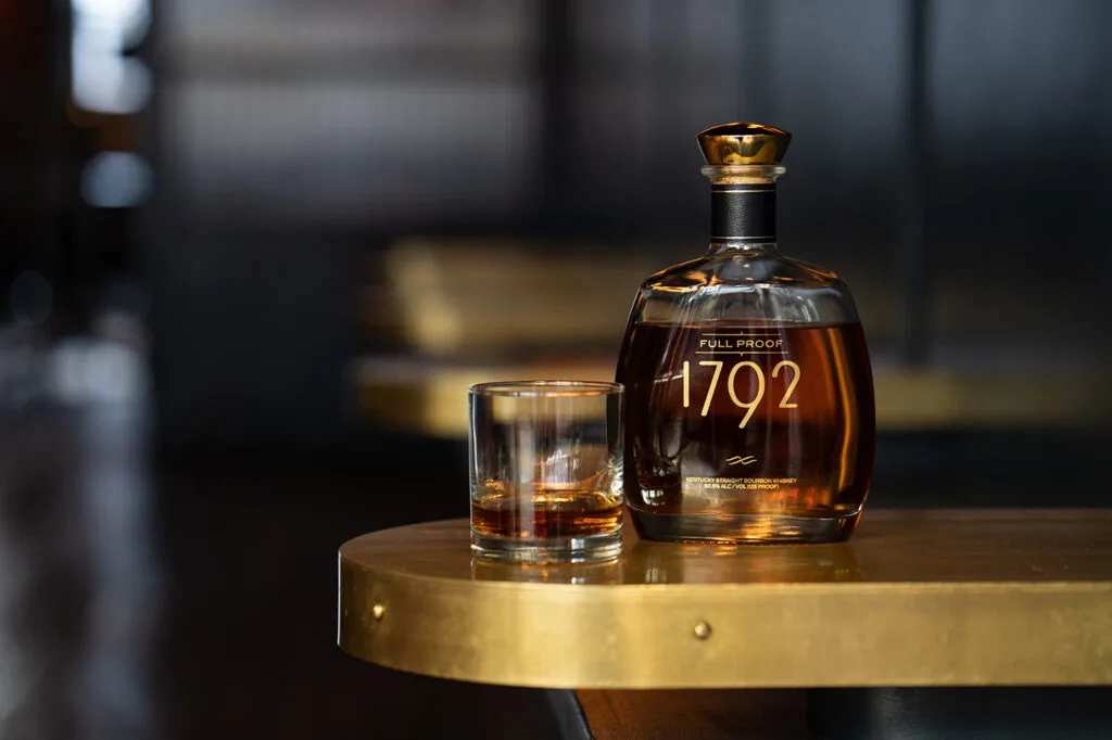 how to do a bourbon tasting - bourbon bottle and glass on brass bar top, credit 1792 style