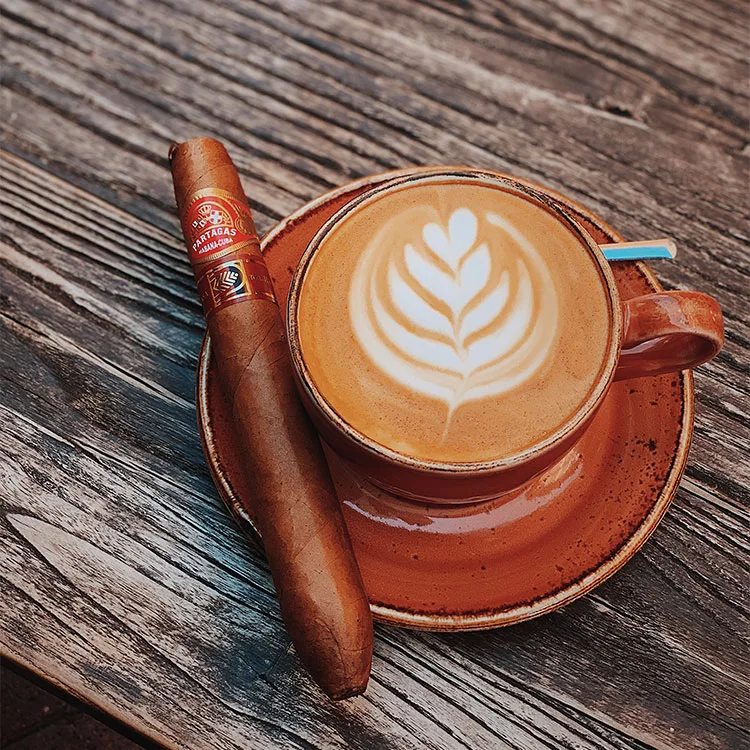 wooden table with latte coffee in orange cup and dish and uncut cigar