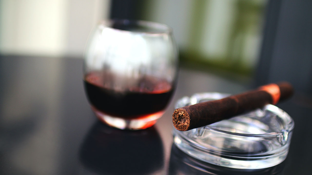 unlit cigar and red wine glass on table with ashtray