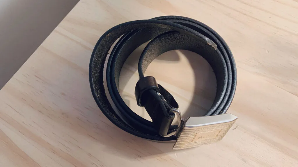 how to store belts - image of rolled up dark brown leather belt on wooden table