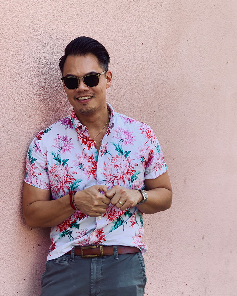 asian man wearing floral shirt in front of light pink wall