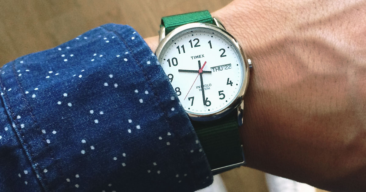 closeup of Timex watch on wrist with green strap and blue long sleeve shirt