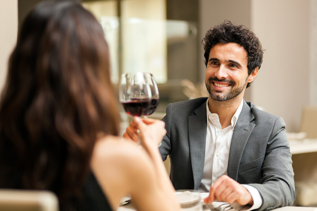 man in grey suit smiling and toasting woman with wine