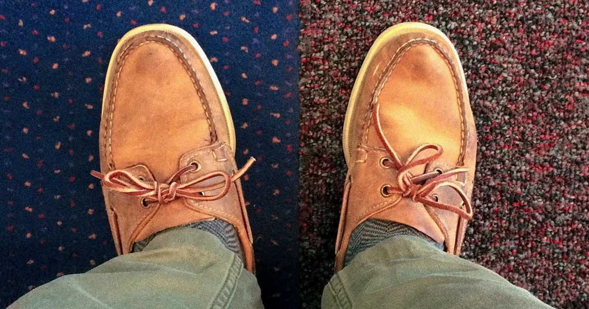 close up of tan boat shoes standing on a blue carpet and a reddish carpet