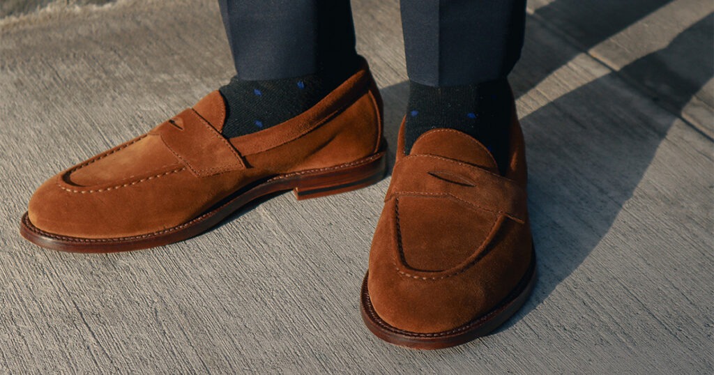 closeup of brown suede loafers and navy pants on sidewalk