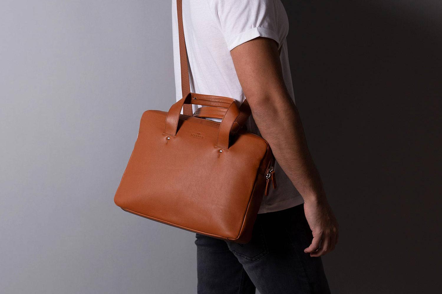 Man in white T-shirt wearing tan leather briefcase. Image via Harber London.
