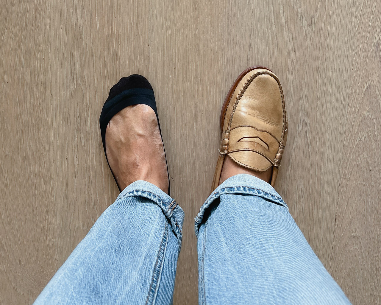 top-down closeup shot of man wearing light blue jeans and one tan loafer on the right foot with one black ondo low cut no show sock on the left foot